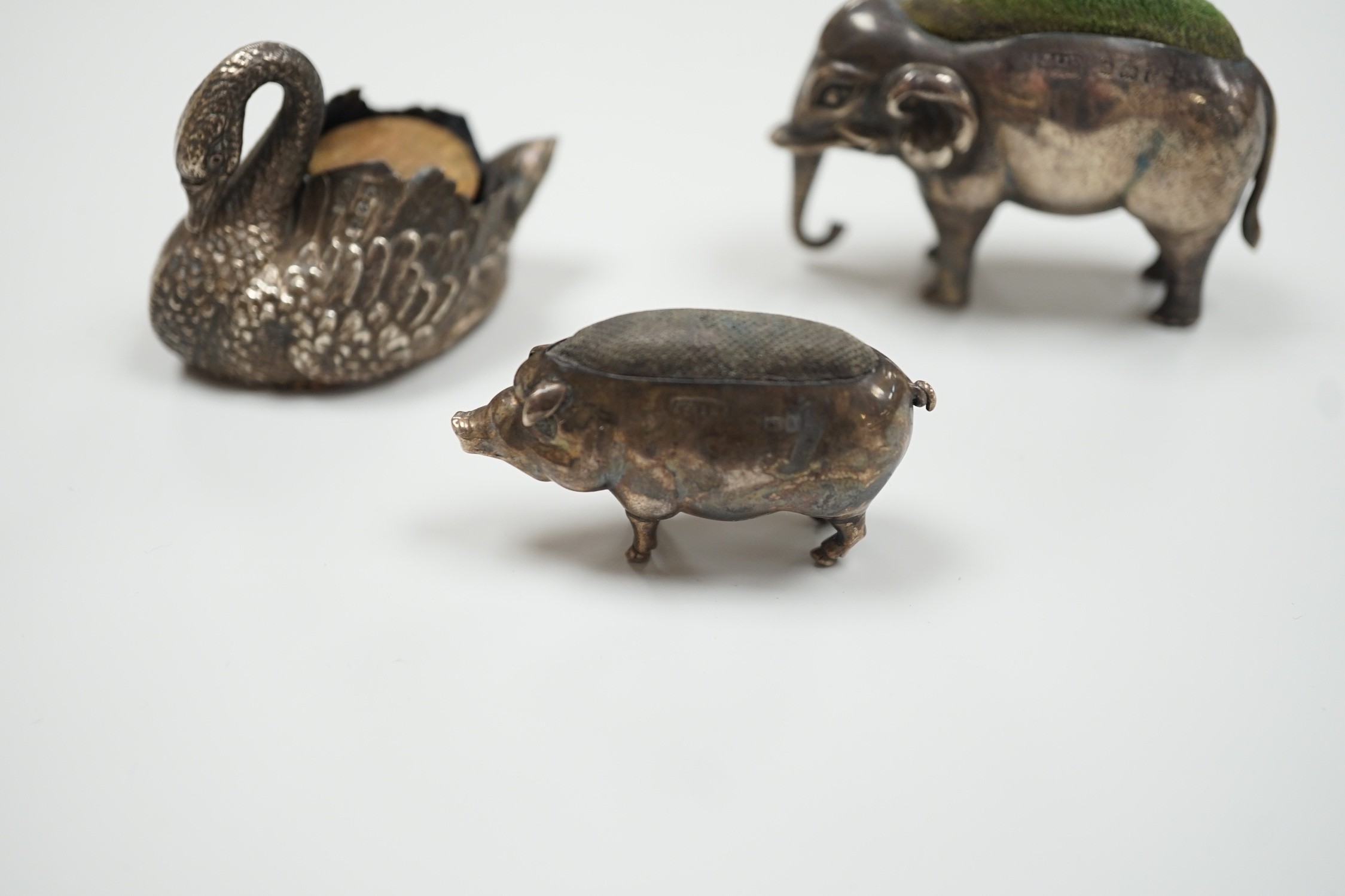 An Edwardian silver elephant pin cushion, Adie & Lovekin, Birmingham, 1905, length 62mm, a similar pig and late Victorian swan pin cushions.